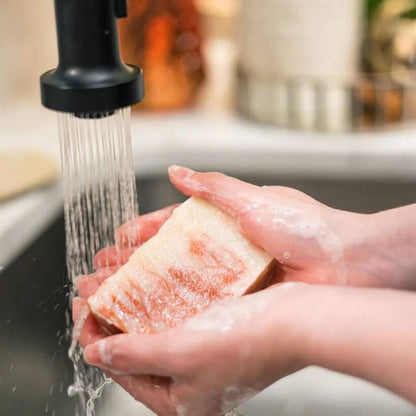 Person holding a piece of Georgia peach soap under running water in a kitchen sink.