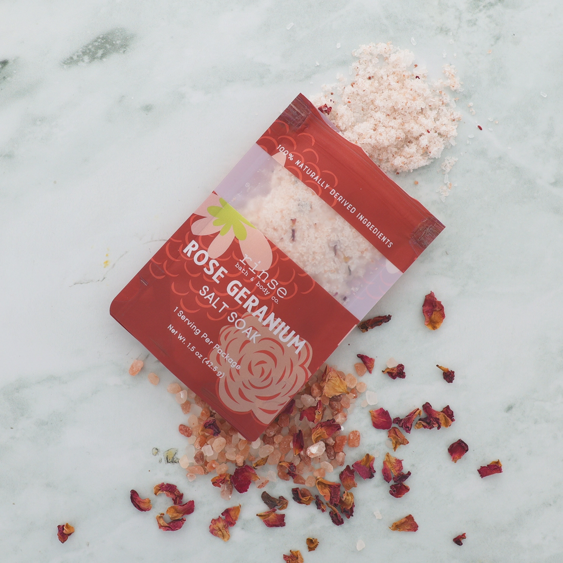 Rose Geranium salt soak packaging with scattered rose petals on a marble surface