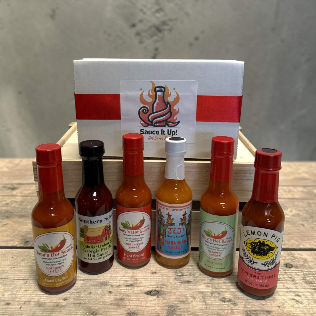 Collection of hot sauce bottles with visible labels on a wooden surface, featuring a branded box in the background.
