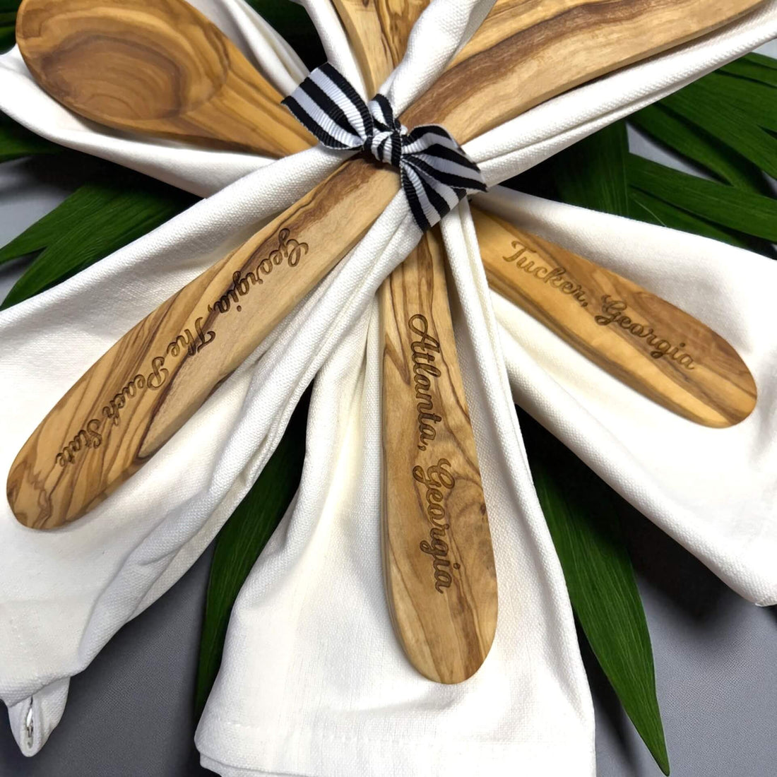 Wooden spoons with engraved text tied together on a white cloth with green leaves in the background