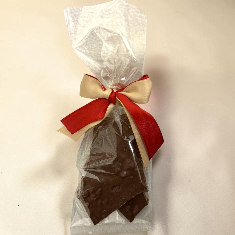 Chocolate toffee bark in a clear cellophane bag tied with a red and beige ribbon, on a plain light background.