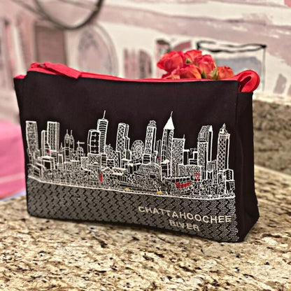 Embroidered black travel bag with white city skyline design and red zipper on a marble surface.