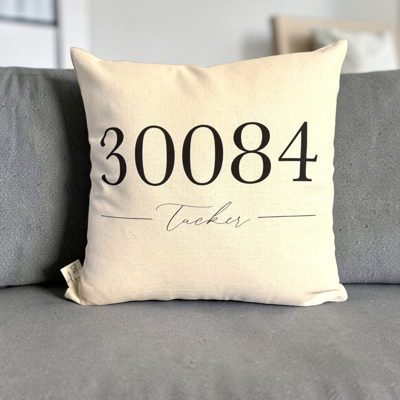 A square cream-colored throw pillow with black printed text reading &