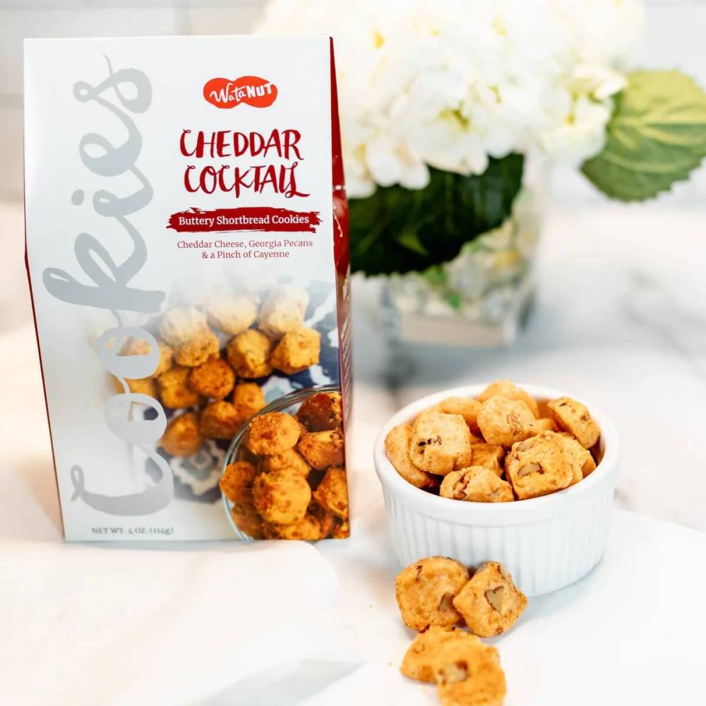 Box of savory cheddar pecan cocktail cookies with bowl of cookies.