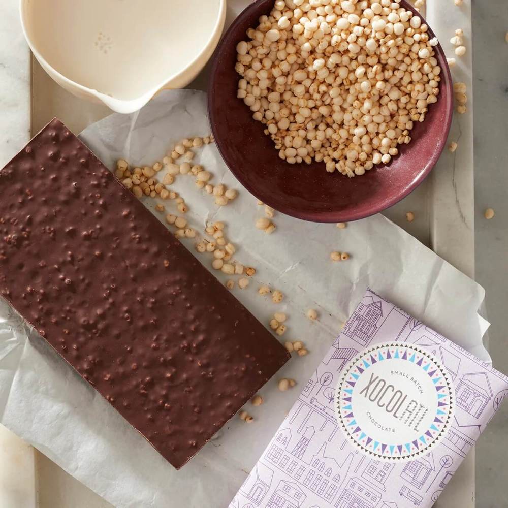 Wrapped and unwrapped bar of dark chocolate surrounded by quinoa puffs and sea salt