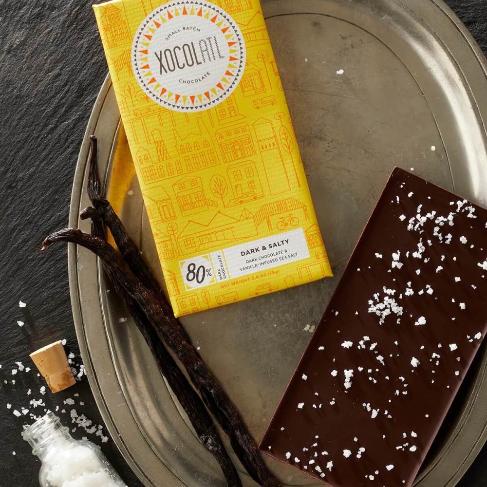 Wrapped and unwrapped bar of dark chocolate with sea salt sprinkled on the back.
