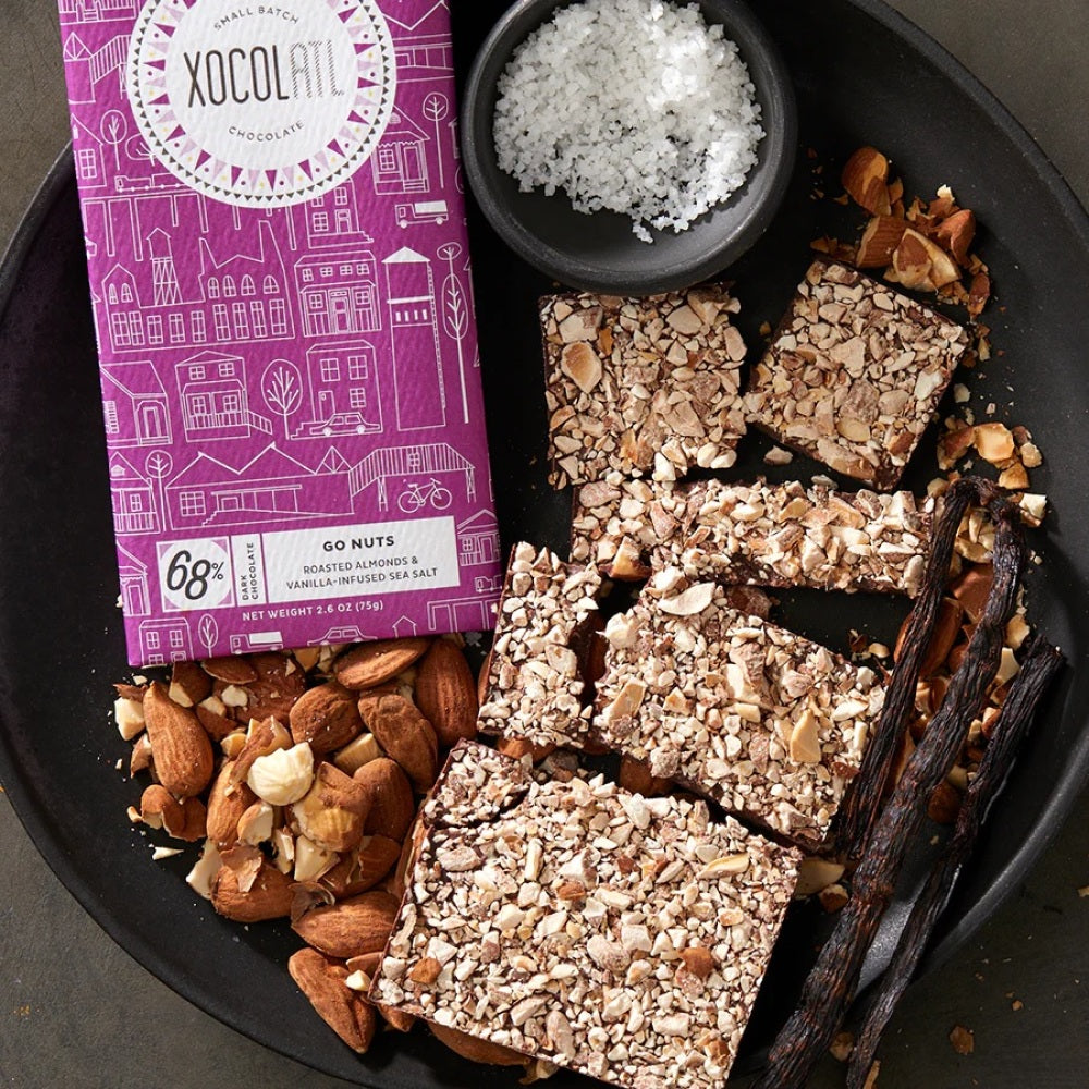 Wrapped and unwrapped bar of dark chocolate covered with chopped almonds