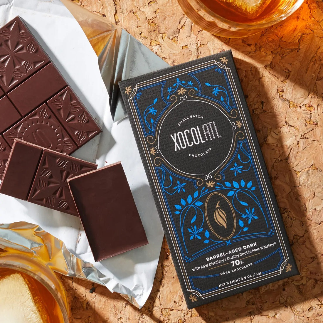 Xocolatl chocolate bar packaging with dark chocolate bars on a cork surface.