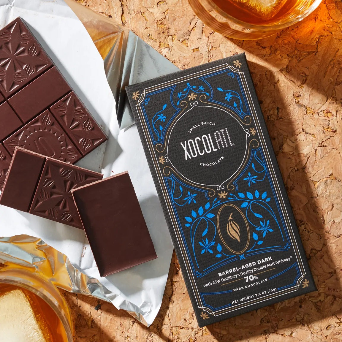 Xocolatl chocolate bar packaging with dark chocolate bars on a cork surface.