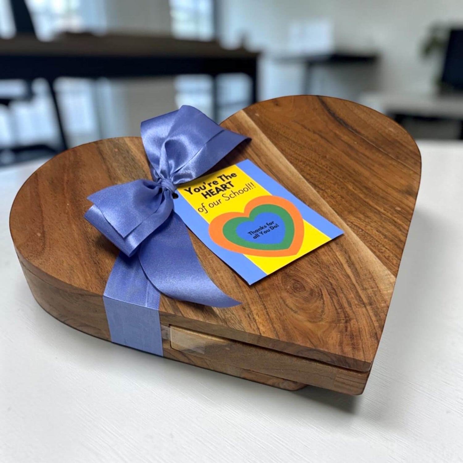 Wooden heart-shaped gift box with a blue ribbon and a card on a white surface.