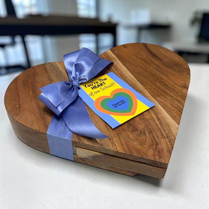 Wooden heart-shaped gift box with a blue ribbon and a card on a white surface.