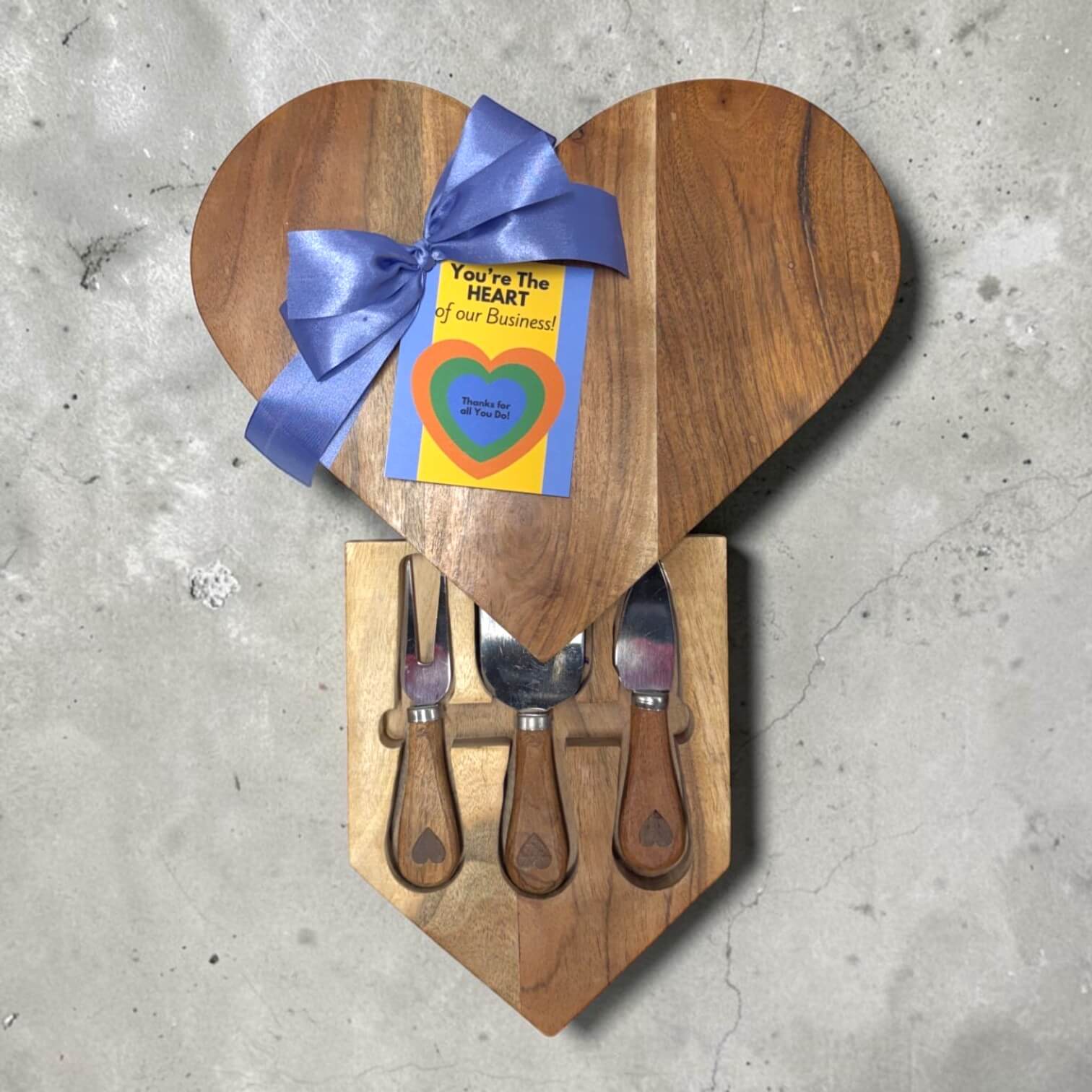 Heart-shaped wooden cutting board with knives and a blue ribbon on a concrete surface